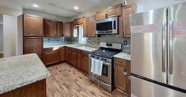 kitchen featuring light stone countertops, appliances with stainless steel finishes, light wood-type flooring, and sink