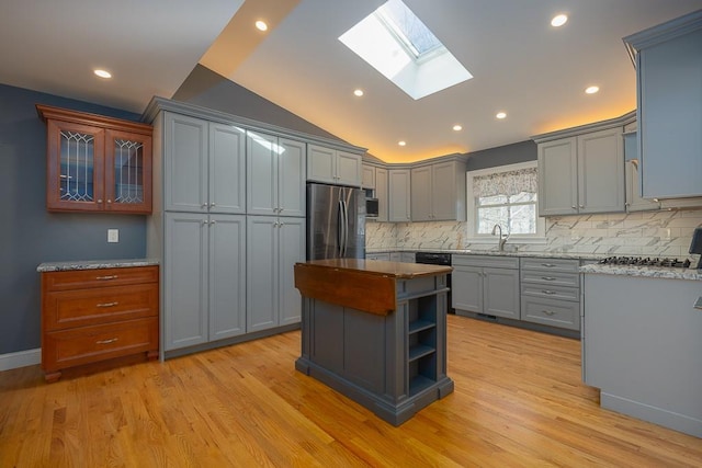 kitchen with tasteful backsplash, lofted ceiling with skylight, light hardwood / wood-style floors, gray cabinets, and appliances with stainless steel finishes