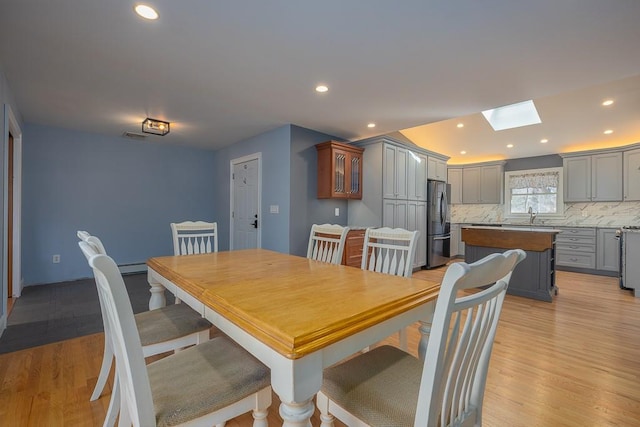 dining space with a baseboard heating unit, a skylight, light hardwood / wood-style floors, and sink