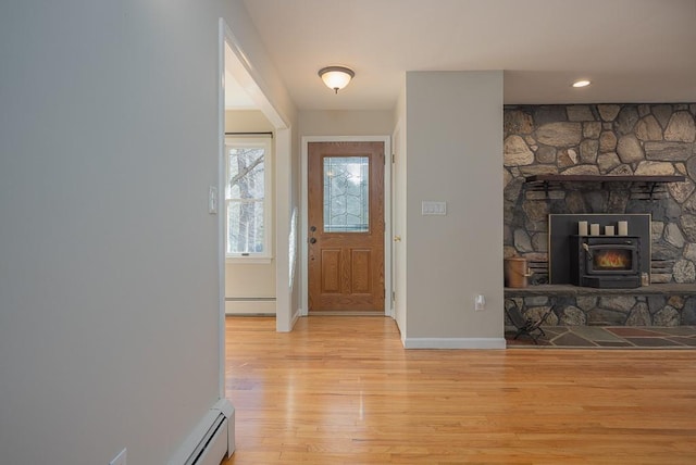 foyer entrance featuring baseboard heating, a wood stove, and light wood-type flooring