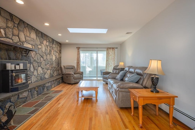 living room featuring baseboard heating, a skylight, light hardwood / wood-style flooring, and a wood stove