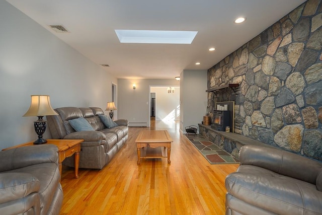 living room featuring light wood-type flooring, a skylight, a wood stove, and a baseboard radiator