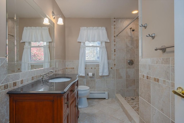 bathroom featuring vanity, a healthy amount of sunlight, baseboard heating, and tile walls