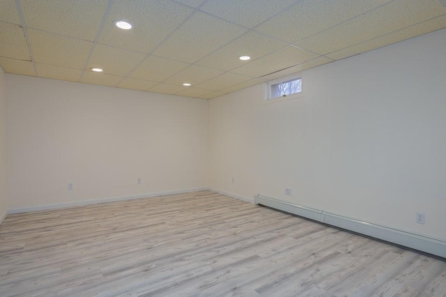 spare room with a drop ceiling, a baseboard radiator, and light hardwood / wood-style flooring