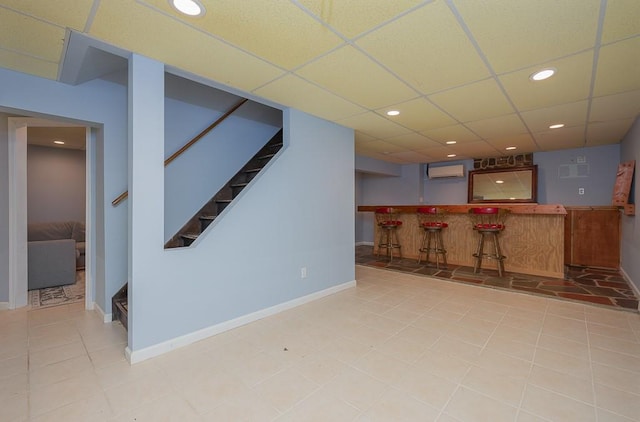 interior space featuring a paneled ceiling, a wall unit AC, light tile patterned floors, and bar