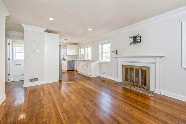 unfurnished living room featuring dark hardwood / wood-style flooring, crown molding, a wealth of natural light, and a brick fireplace