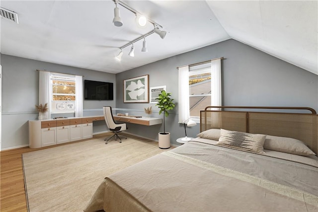 bedroom with built in desk, light wood-type flooring, multiple windows, and lofted ceiling