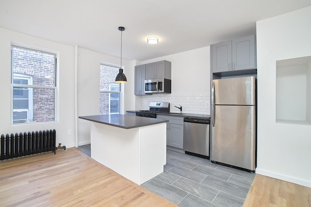 kitchen with light wood-type flooring, stainless steel appliances, decorative light fixtures, radiator heating unit, and gray cabinets