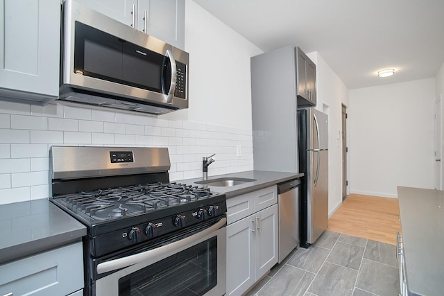 kitchen with tasteful backsplash, gray cabinetry, stainless steel appliances, sink, and light hardwood / wood-style floors