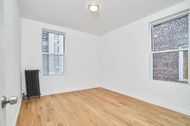 empty room featuring radiator, plenty of natural light, and light hardwood / wood-style floors