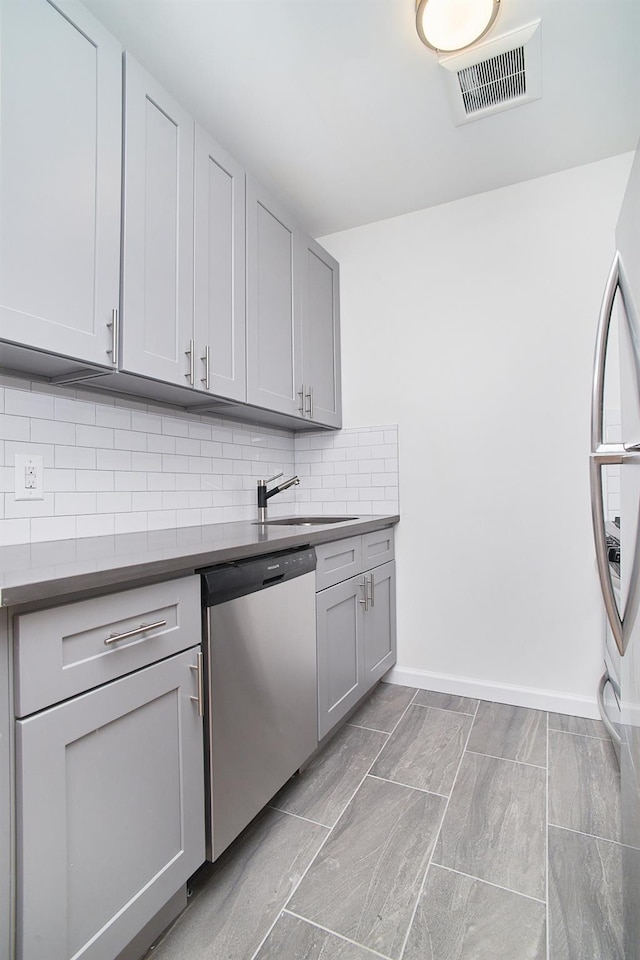 kitchen featuring decorative backsplash, appliances with stainless steel finishes, gray cabinetry, and sink