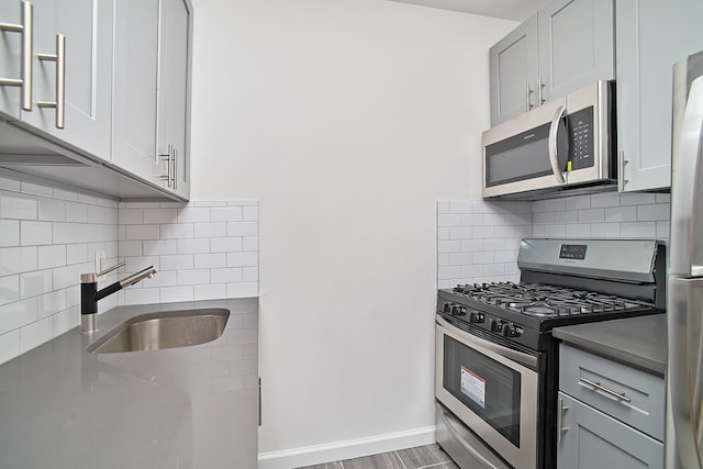 kitchen featuring sink, dark hardwood / wood-style floors, backsplash, gray cabinets, and appliances with stainless steel finishes