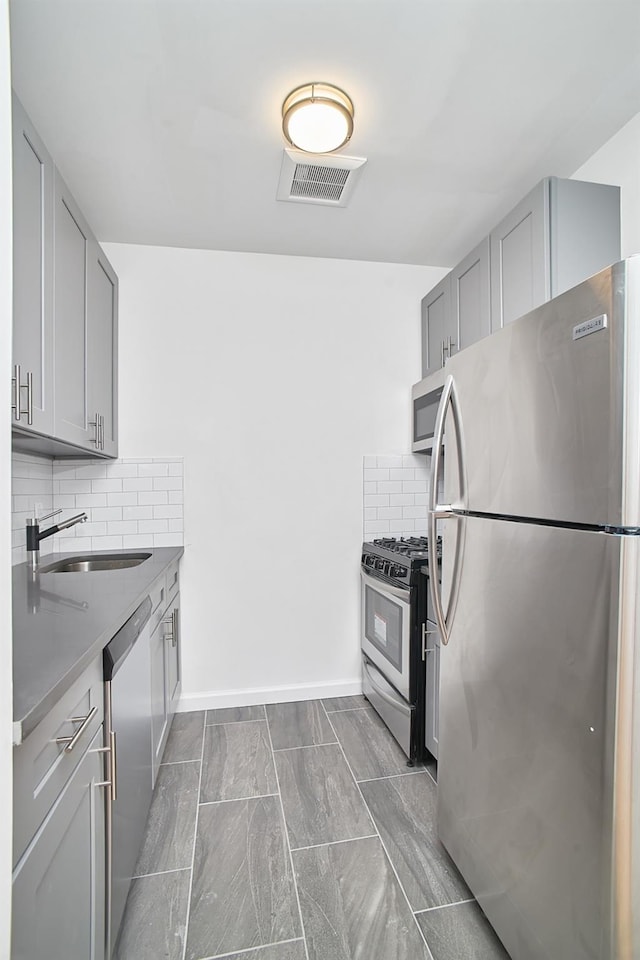 kitchen featuring gray cabinetry, sink, appliances with stainless steel finishes, and tasteful backsplash