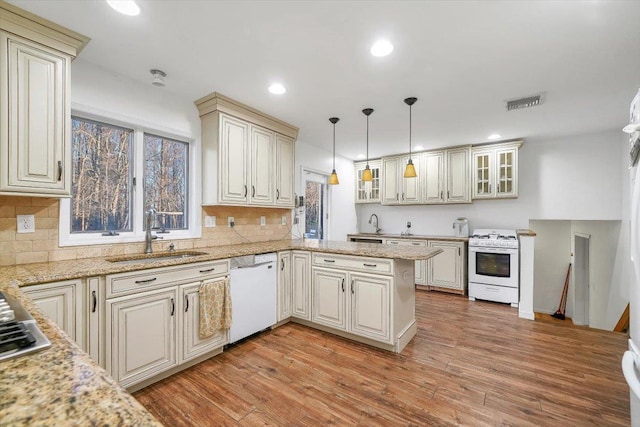 kitchen with sink, kitchen peninsula, pendant lighting, white appliances, and light hardwood / wood-style floors