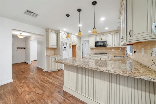 kitchen with kitchen peninsula, light stone countertops, sink, light hardwood / wood-style floors, and hanging light fixtures