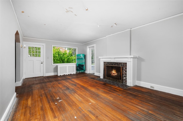 unfurnished living room featuring arched walkways, radiator heating unit, a brick fireplace, baseboards, and hardwood / wood-style flooring