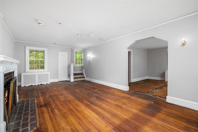 unfurnished living room featuring a warm lit fireplace, arched walkways, baseboards, radiator heating unit, and ornamental molding