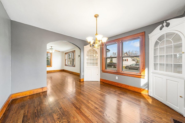 unfurnished dining area with ceiling fan with notable chandelier and dark hardwood / wood-style floors