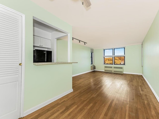 unfurnished living room with dark hardwood / wood-style floors, track lighting, radiator, and ceiling fan