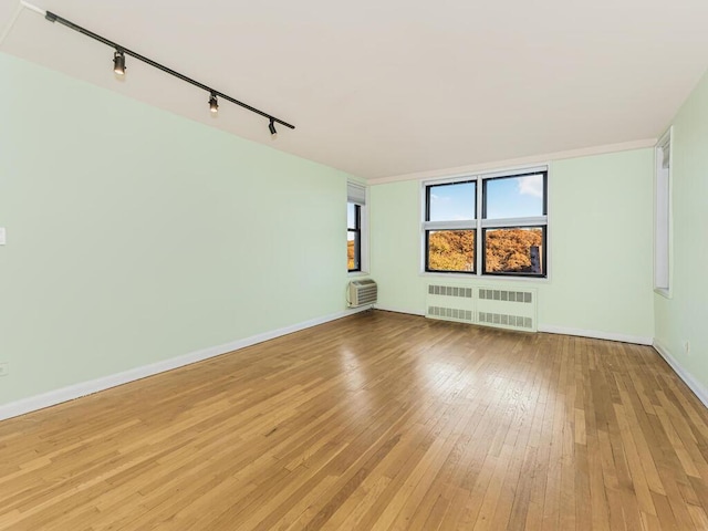 unfurnished room with a wall mounted air conditioner, track lighting, light hardwood / wood-style flooring, and radiator