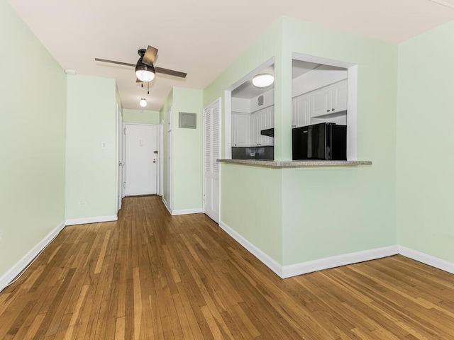 interior space with white cabinetry, ceiling fan, black fridge, kitchen peninsula, and wood-type flooring