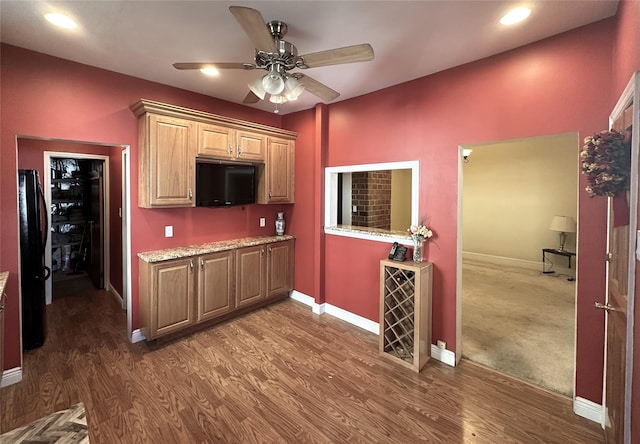 kitchen featuring dark hardwood / wood-style floors, ceiling fan, black fridge, and light stone countertops