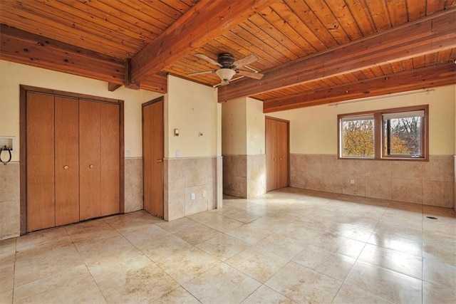 empty room with wood ceiling, ceiling fan, light tile patterned floors, tile walls, and beamed ceiling