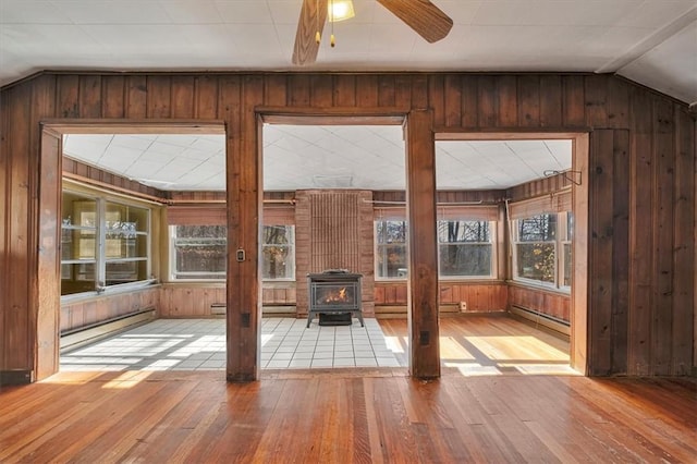 unfurnished sunroom with a baseboard radiator, a wood stove, ceiling fan, and lofted ceiling