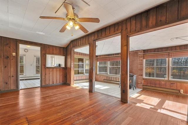 unfurnished sunroom with a wood stove, ceiling fan, vaulted ceiling, and a baseboard heating unit