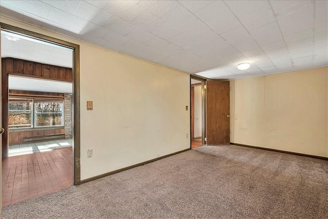 spare room featuring carpet flooring, wood walls, and baseboard heating