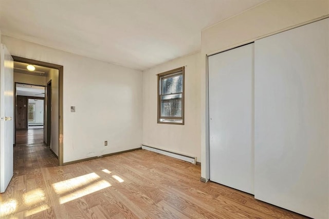 unfurnished bedroom featuring a closet, light hardwood / wood-style flooring, and a baseboard heating unit