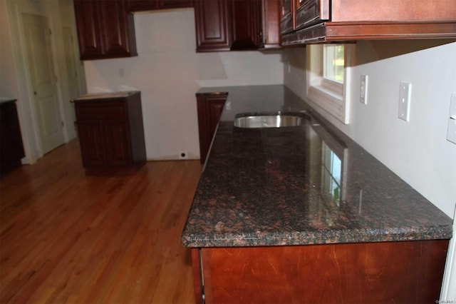 kitchen with hardwood / wood-style flooring, dark stone countertops, and sink