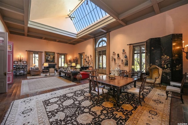 dining room with hardwood / wood-style floors, a towering ceiling, a healthy amount of sunlight, and coffered ceiling