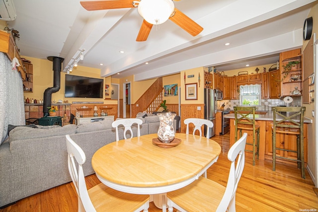 dining room with a wood stove, light hardwood / wood-style flooring, ceiling fan, beam ceiling, and a wall unit AC