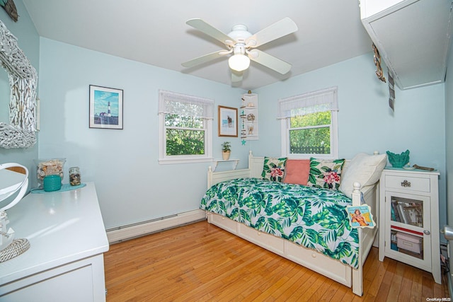 bedroom featuring multiple windows, ceiling fan, light wood-type flooring, and a baseboard heating unit