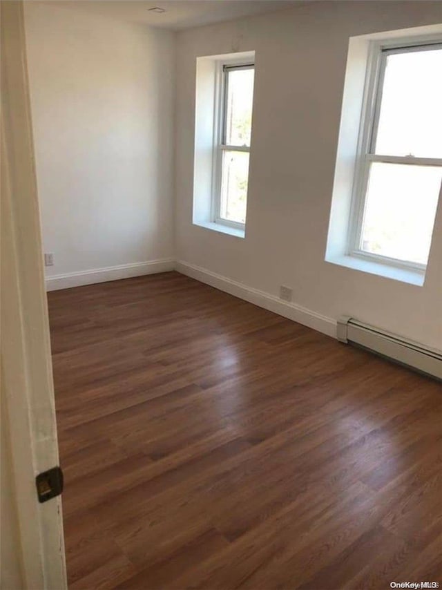 spare room with a healthy amount of sunlight, dark hardwood / wood-style flooring, and a baseboard radiator