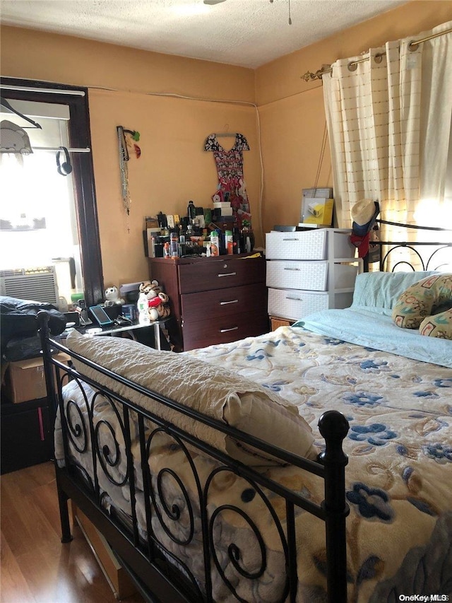 bedroom featuring light hardwood / wood-style floors, a textured ceiling, and cooling unit