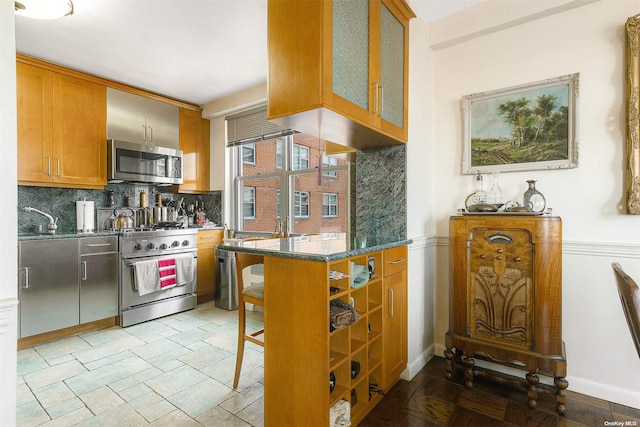 kitchen with decorative backsplash, kitchen peninsula, dark stone counters, stainless steel appliances, and sink