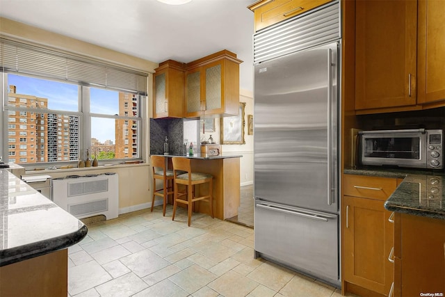 kitchen with backsplash, stainless steel built in fridge, dark stone countertops, and heating unit