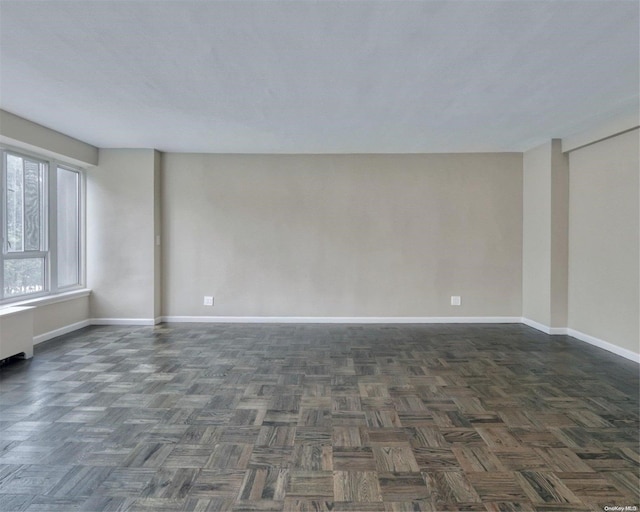 empty room with dark parquet flooring and radiator