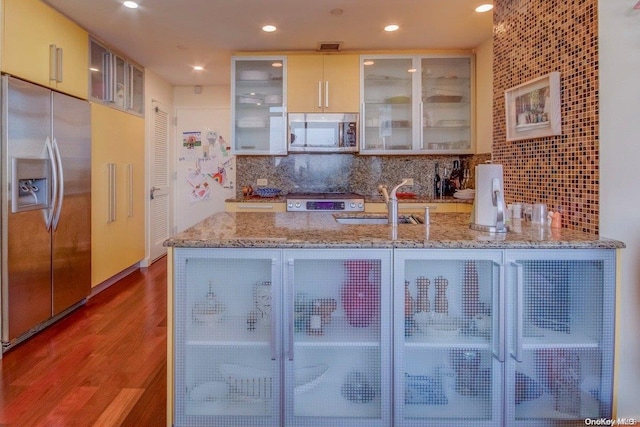 kitchen featuring sink, stainless steel appliances, light stone counters, backsplash, and hardwood / wood-style floors