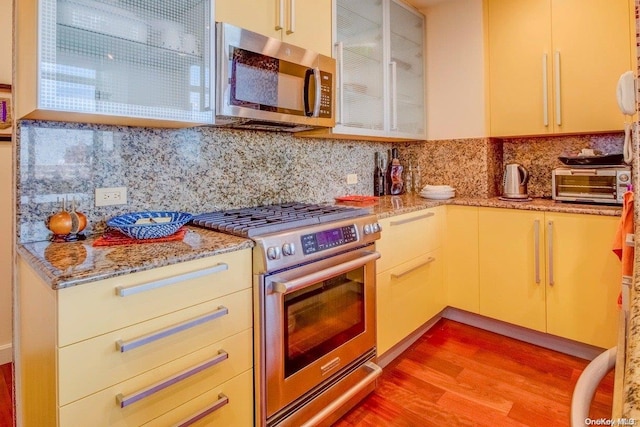 kitchen featuring decorative backsplash, appliances with stainless steel finishes, light hardwood / wood-style floors, and light stone counters