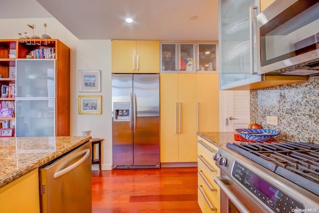 kitchen featuring decorative backsplash, light stone countertops, stainless steel appliances, and light wood-type flooring