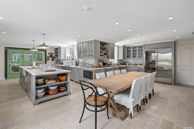 kitchen with gray cabinetry, built in appliances, light stone countertops, decorative light fixtures, and a kitchen island