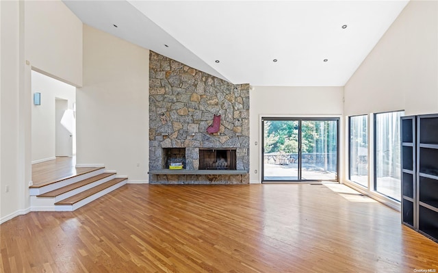 unfurnished living room with light hardwood / wood-style floors, a stone fireplace, and high vaulted ceiling