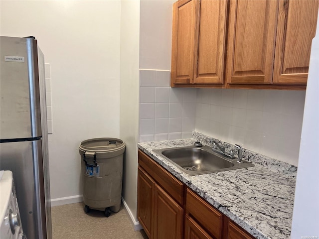 kitchen with light stone counters, tasteful backsplash, stainless steel refrigerator, and sink