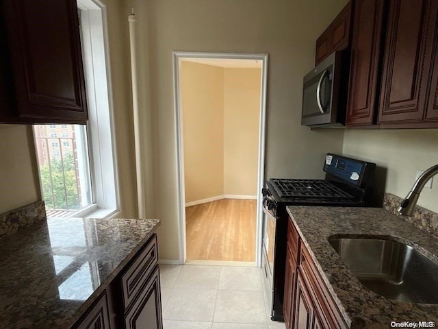 kitchen featuring light tile patterned flooring, dark stone countertops, black range oven, and sink