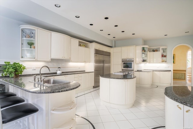 kitchen featuring a kitchen bar, sink, dark stone countertops, a kitchen island, and stainless steel appliances