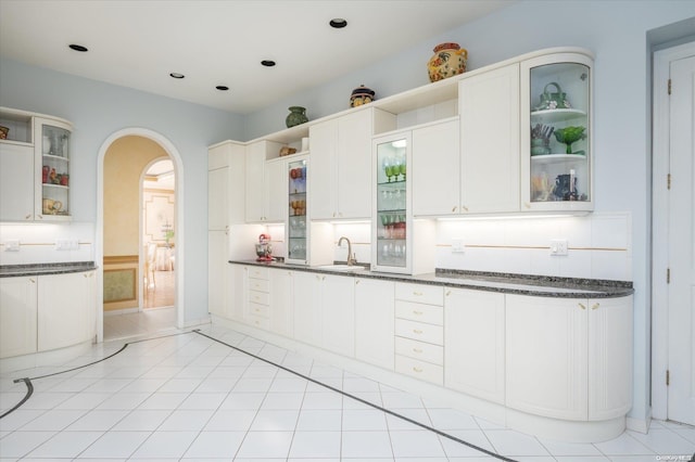 kitchen featuring dark stone countertops, sink, light tile patterned floors, and white cabinets