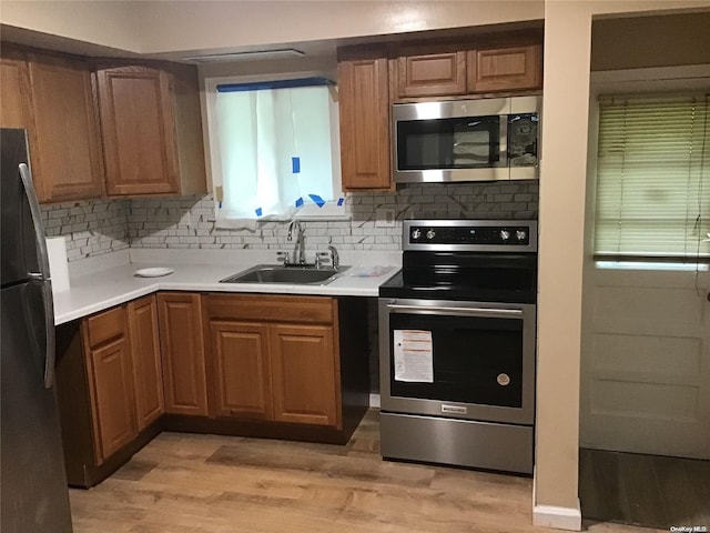 kitchen with appliances with stainless steel finishes, light wood-type flooring, backsplash, and sink